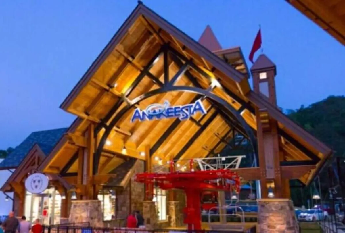 A large wooden structure with a brightly lit sign and the iconic red gondola lift, set against greenery and open sky. Families can be seen exploring the lively park atmosphere, hinting at the thrill and fun of Anakeesta’s attractions, including scenic rides and mountaintop play areas.
