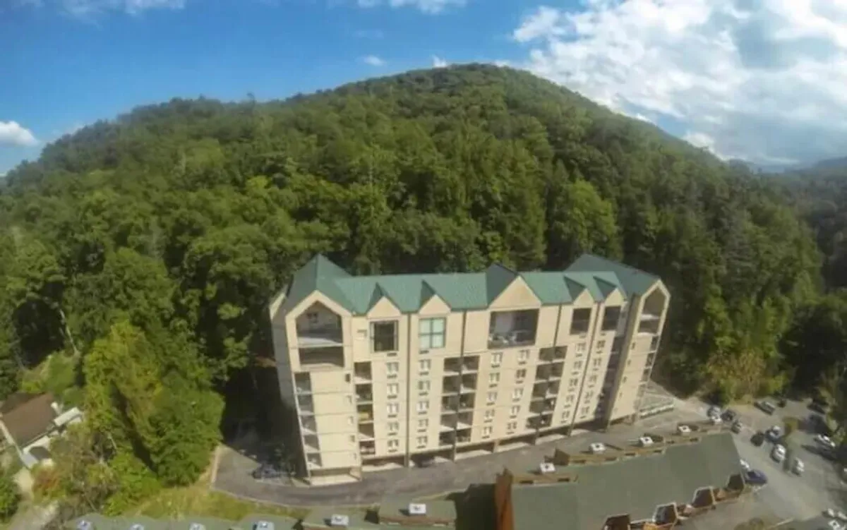 This exterior shot captures the multi-story condo building surrounded by lush greenery and a mountainous backdrop. The tranquil setting highlights the convenience of returning to a comfortable home base after a day of exploring local family attractions.