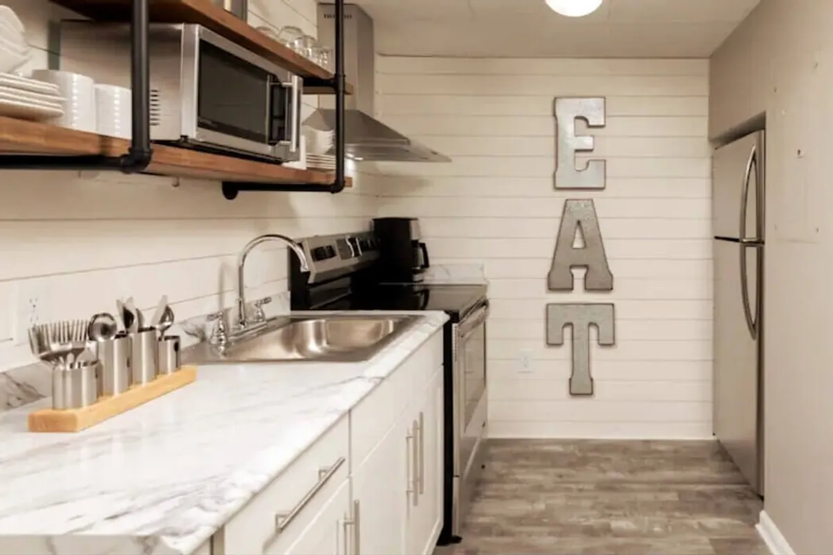 A cozy, welcoming kitchen with a marble countertop at center, bold 'EAT' wall art, and gleaming stainless steel appliances. The space is well-lit and designed for both cooking and social interaction, illustrating a warm, contemporary environment ideal for meal preparation and gathering.