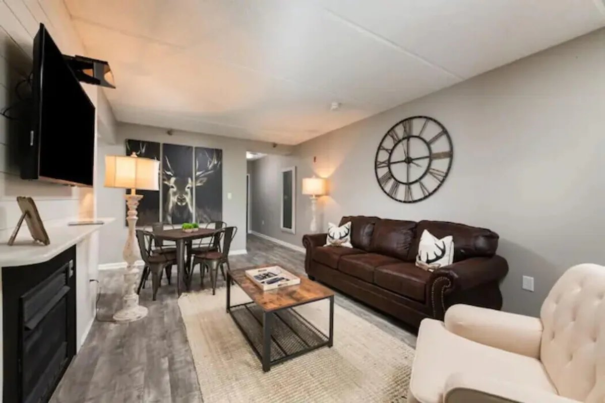 This image showcases an open-concept living and dining room with a leather couch, a dining table, a wall clock, and artwork on the wall. There is ample space for relaxing, socializing, watching TV, and dining. The decor and furniture create a cozy, welcoming atmosphere.