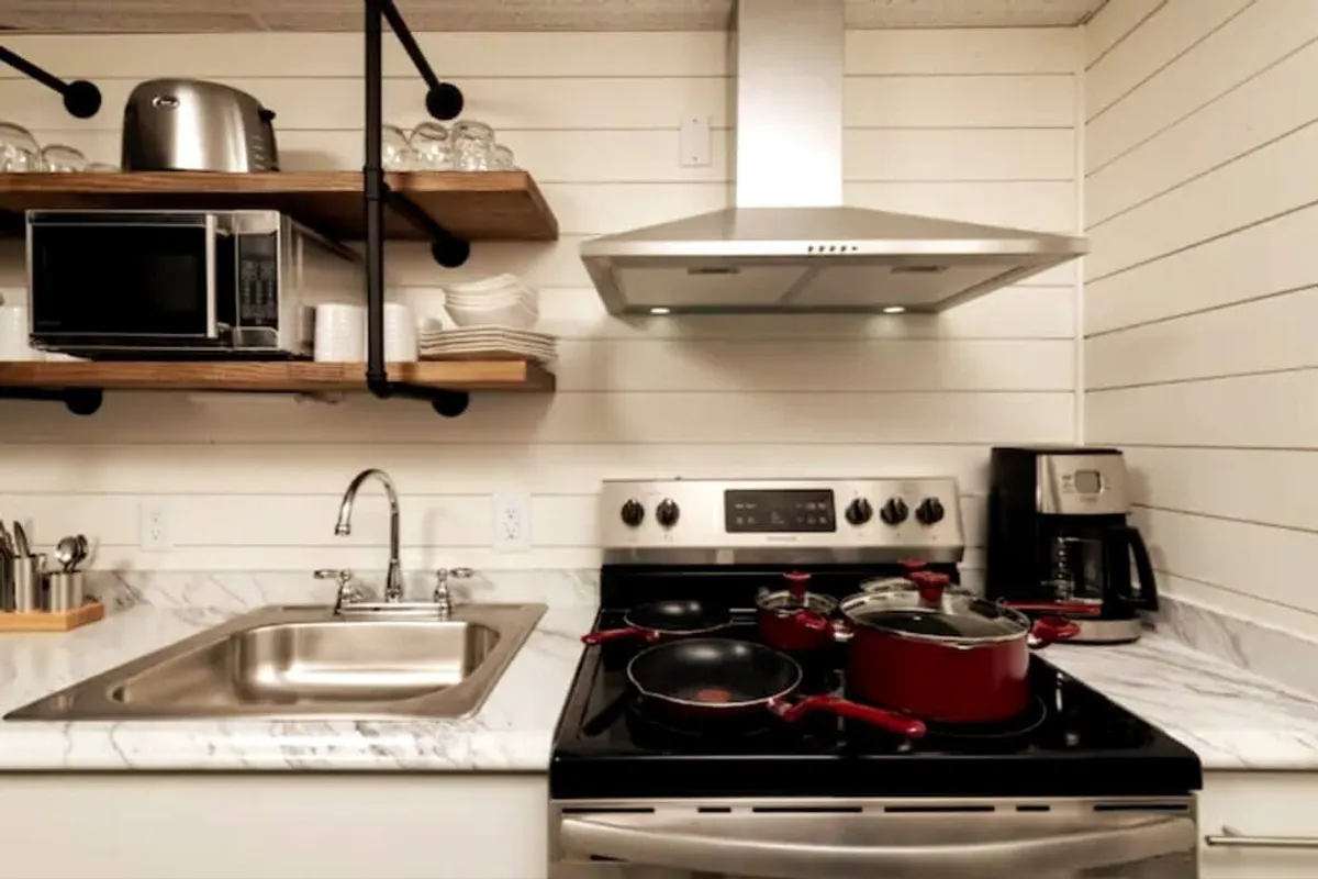 A stylish kitchen scene featuring a marble countertop, vibrant red cookware, and open shelving displaying dishes. The arrangement is functional and visually appealing, underscoring the kitchen’s capacity for hosting gatherings and preparing meals in an inviting, modern space.