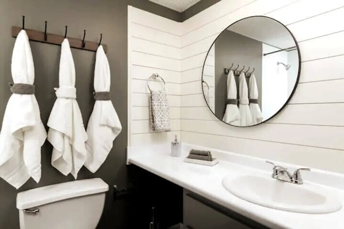 A serene bathroom scene with a round mirror, neatly arranged towels, and a modern sink. The space is clean, inviting, and designed for personal comfort and relaxation.