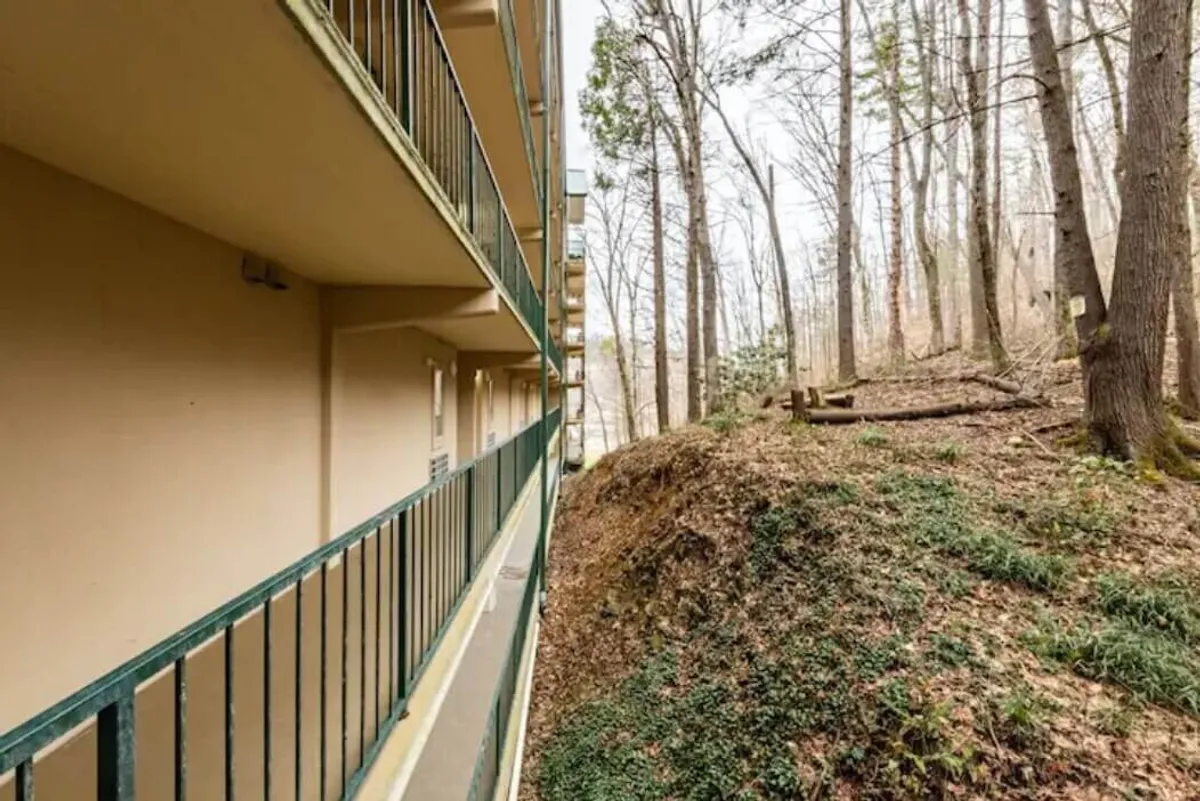 A peaceful balcony view with a railing overlooking a backdrop of trees and the building facade. The setting is serene, inviting residents to enjoy nature, relax outdoors, or sip coffee while soaking in the surroundings.
