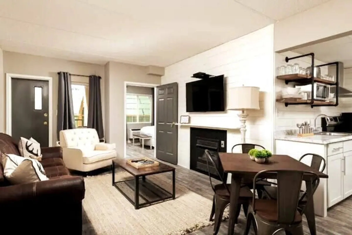A comfortable living area featuring a leather sofa, a white armchair, a coffee table, and a TV stand. The space is arranged for socializing, relaxing, and enjoying entertainment. Natural light streams in, suggesting the presence of large windows.